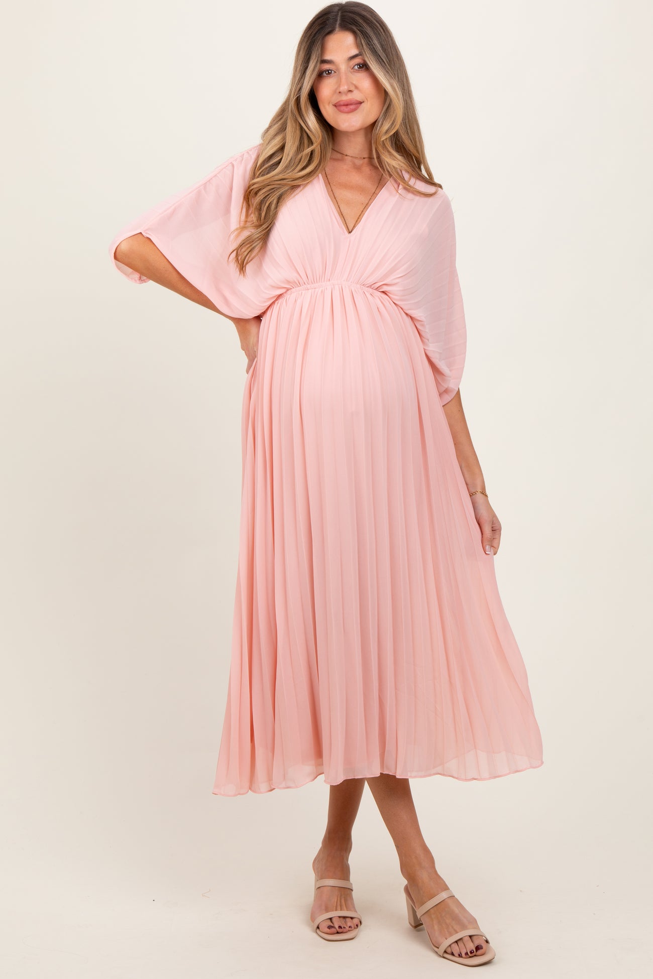 woman wearing a light pink pleated maternity dress with a v-neckline and a visible baby bump
