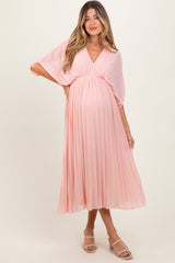 woman wearing a light pink pleated maternity dress with a v-neckline and a visible baby bump