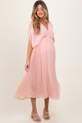 woman wearing a light pink pleated maternity dress with a v-neckline and flowing sleeves, showcasing her baby bump