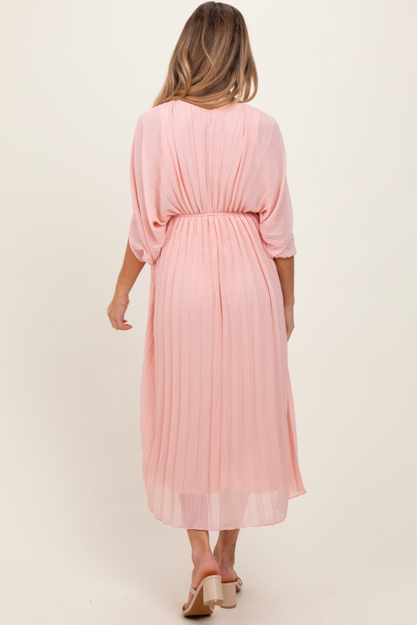 woman wearing a light pink pleated maternity dress shown from the back