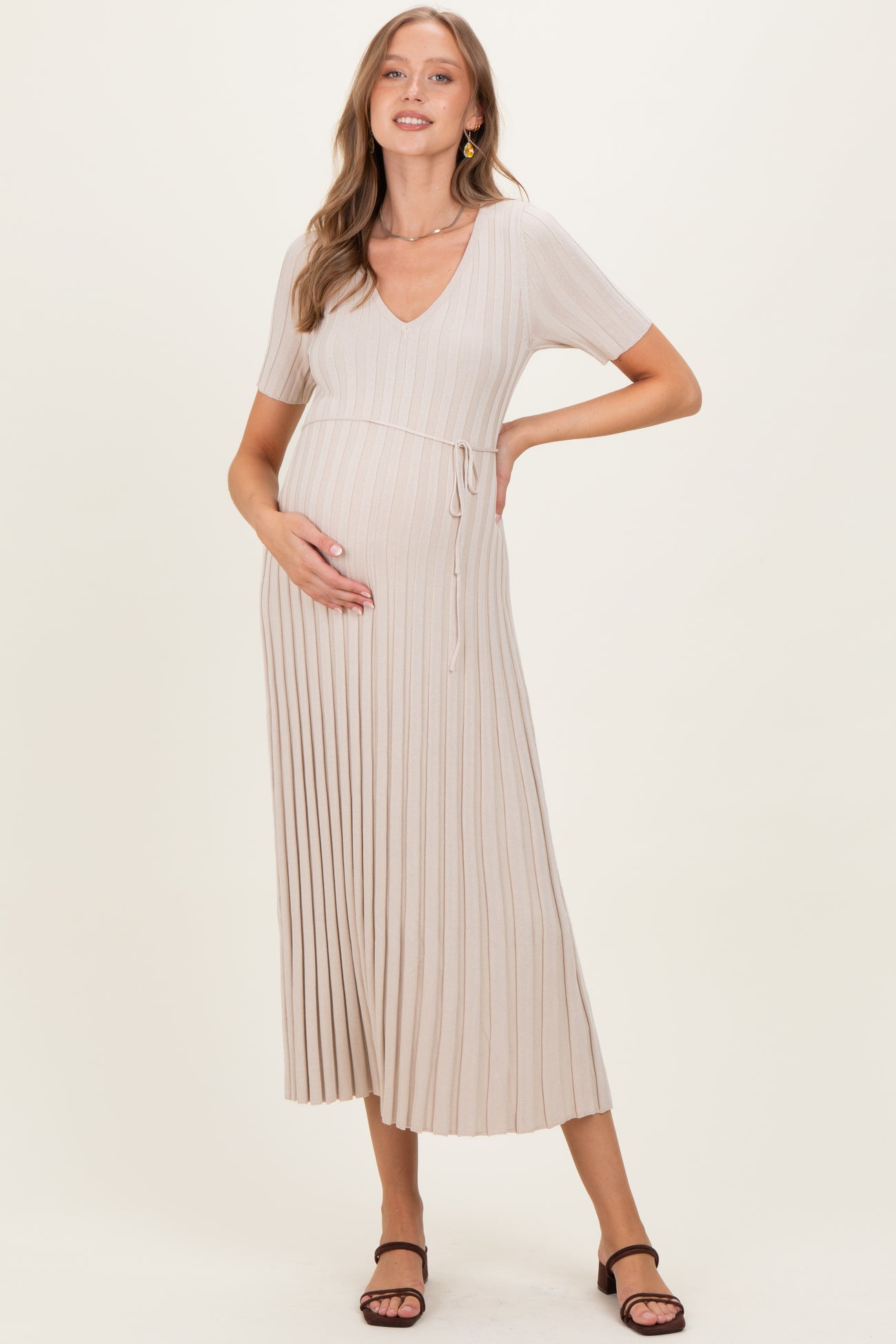 woman wearing a beige ribbed maternity dress with a v-neck and short sleeves, holding her baby bump