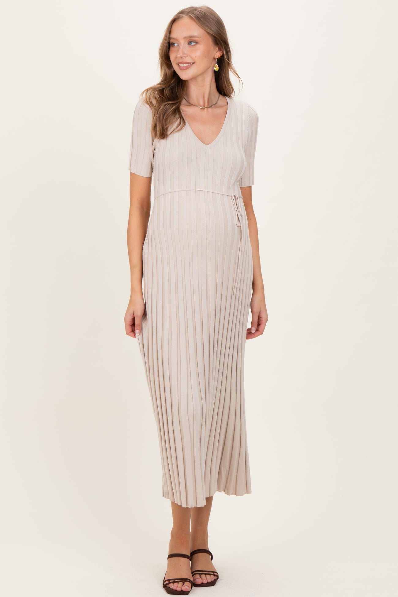 woman wearing a beige maternity dress with short sleeves and a v-neck, featuring a pleated design and a baby bump visible