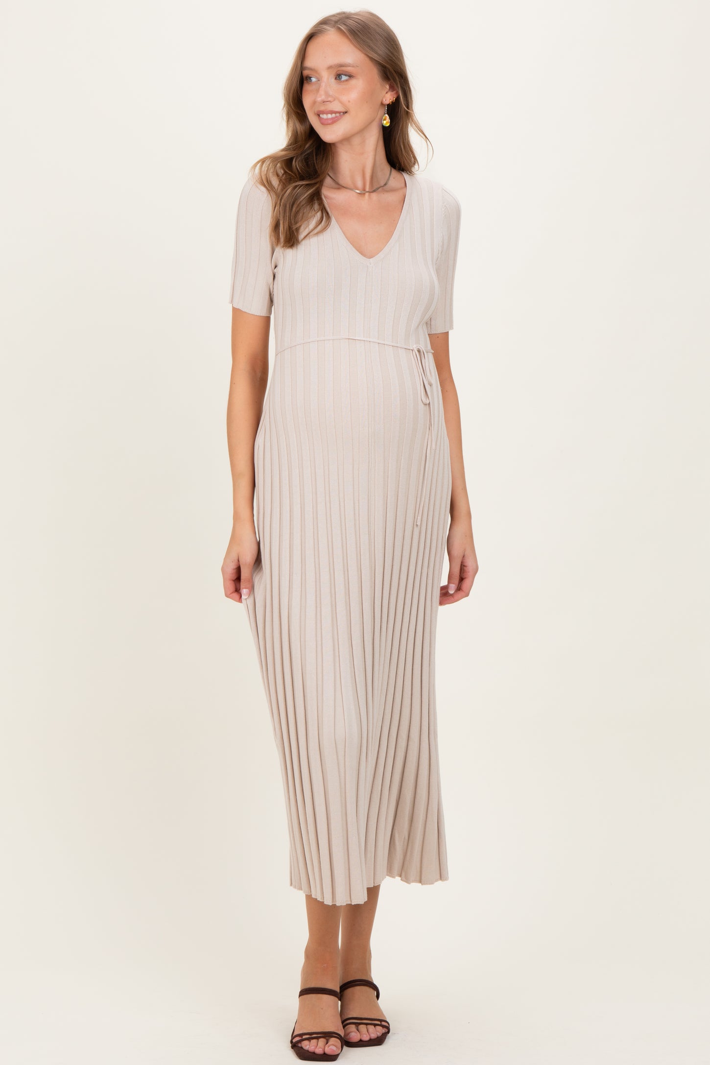 woman wearing a beige maternity dress with short sleeves and a v-neck, featuring a pleated design and a baby bump visible