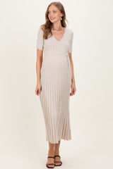 woman wearing a beige maternity dress with short sleeves and a v-neck, featuring a pleated design and a baby bump visible