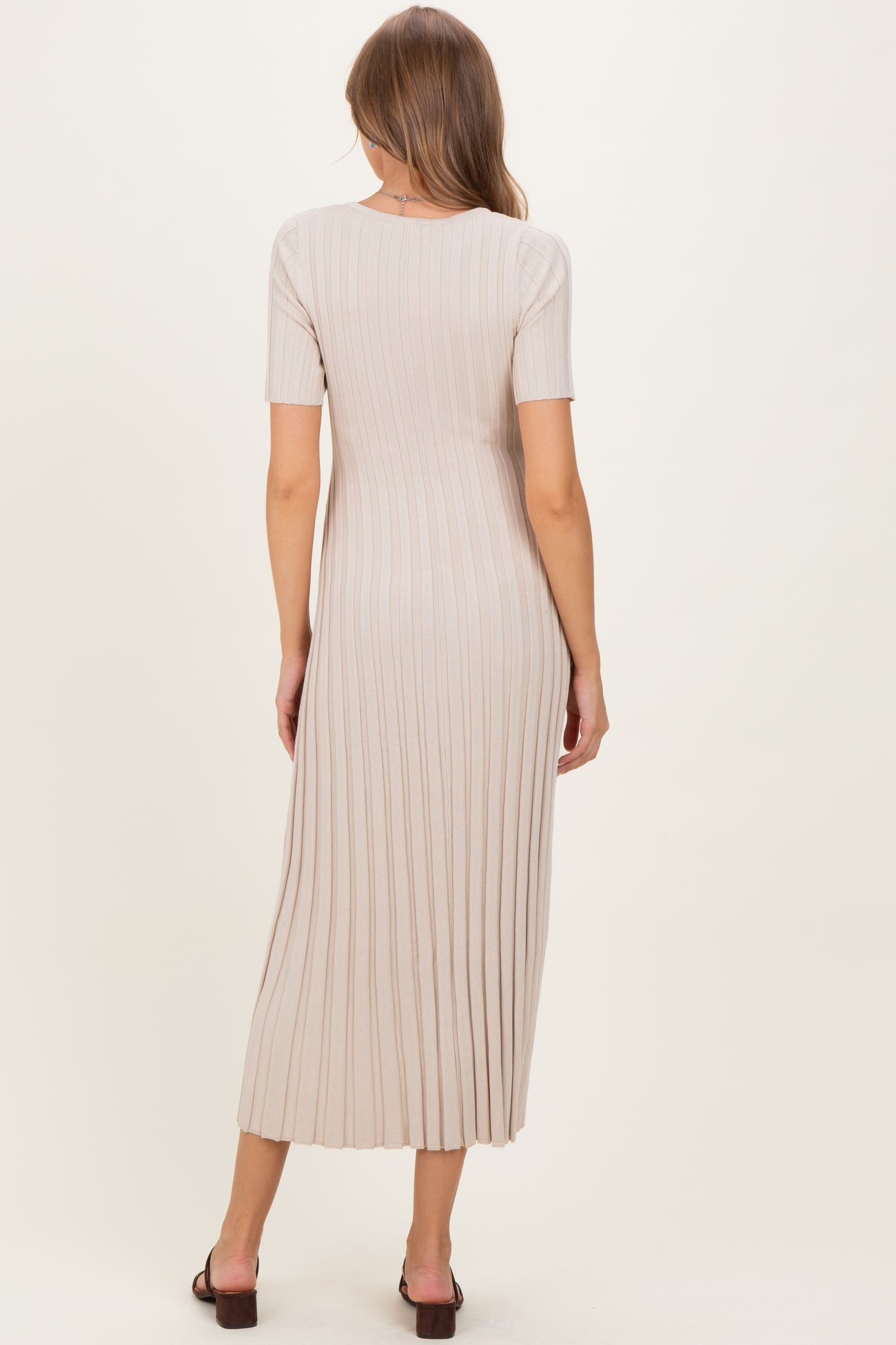 woman wearing a beige ribbed maternity dress with short sleeves and a midi length, showing a relaxed fit and a baby bump