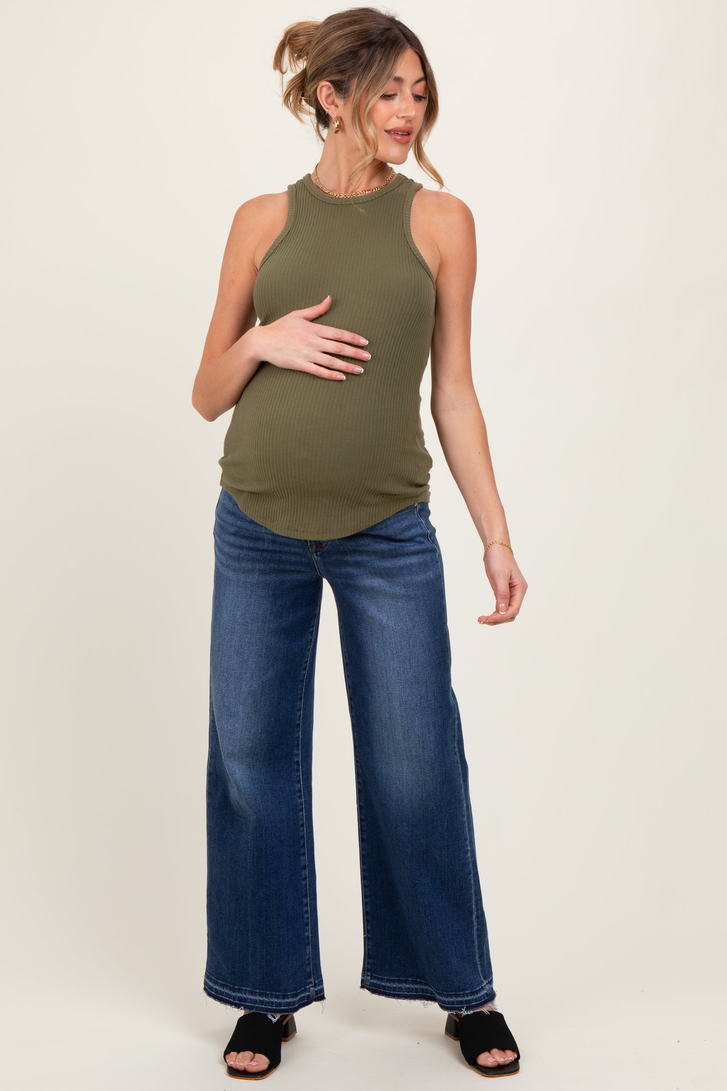 woman wearing a dark green ribbed maternity tank top and wide leg jeans, holding her baby bump
