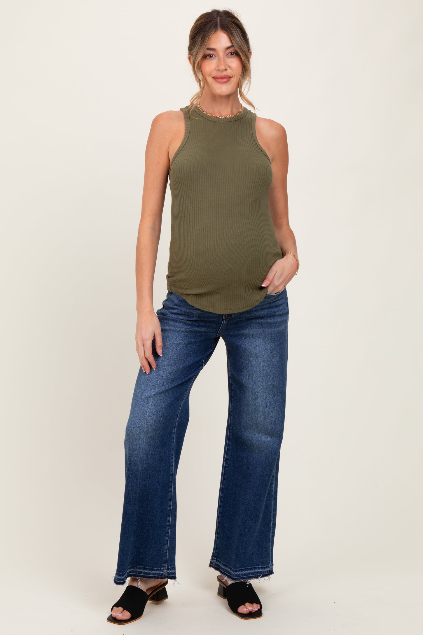 woman wearing an olive green ribbed maternity tank top and blue wide-leg maternity jeans, showing her baby bump