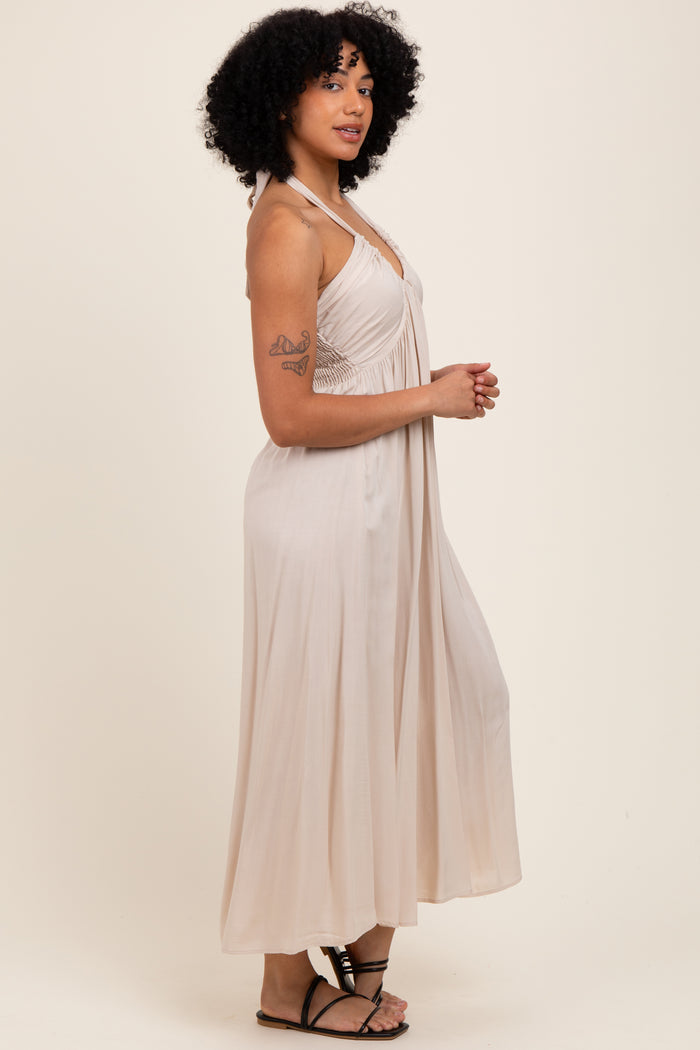 woman wearing a beige halter neck maxi dress with a flowy silhouette and a fitted bodice