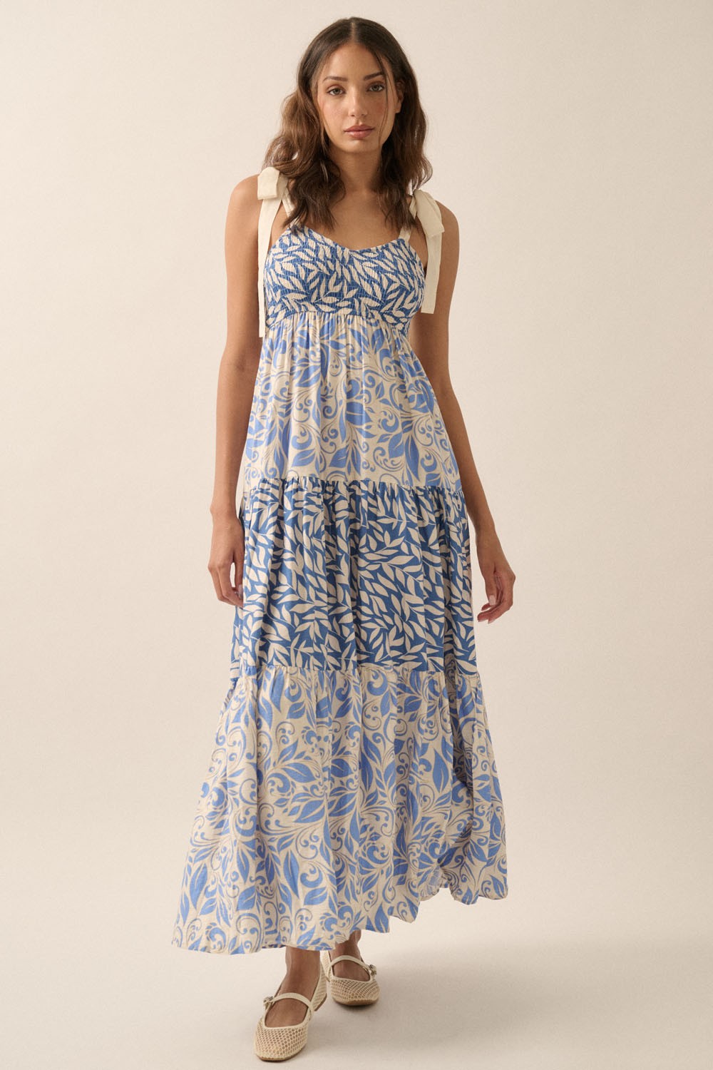 woman wearing a floral blue and cream maxi dress with tie straps and a tiered skirt