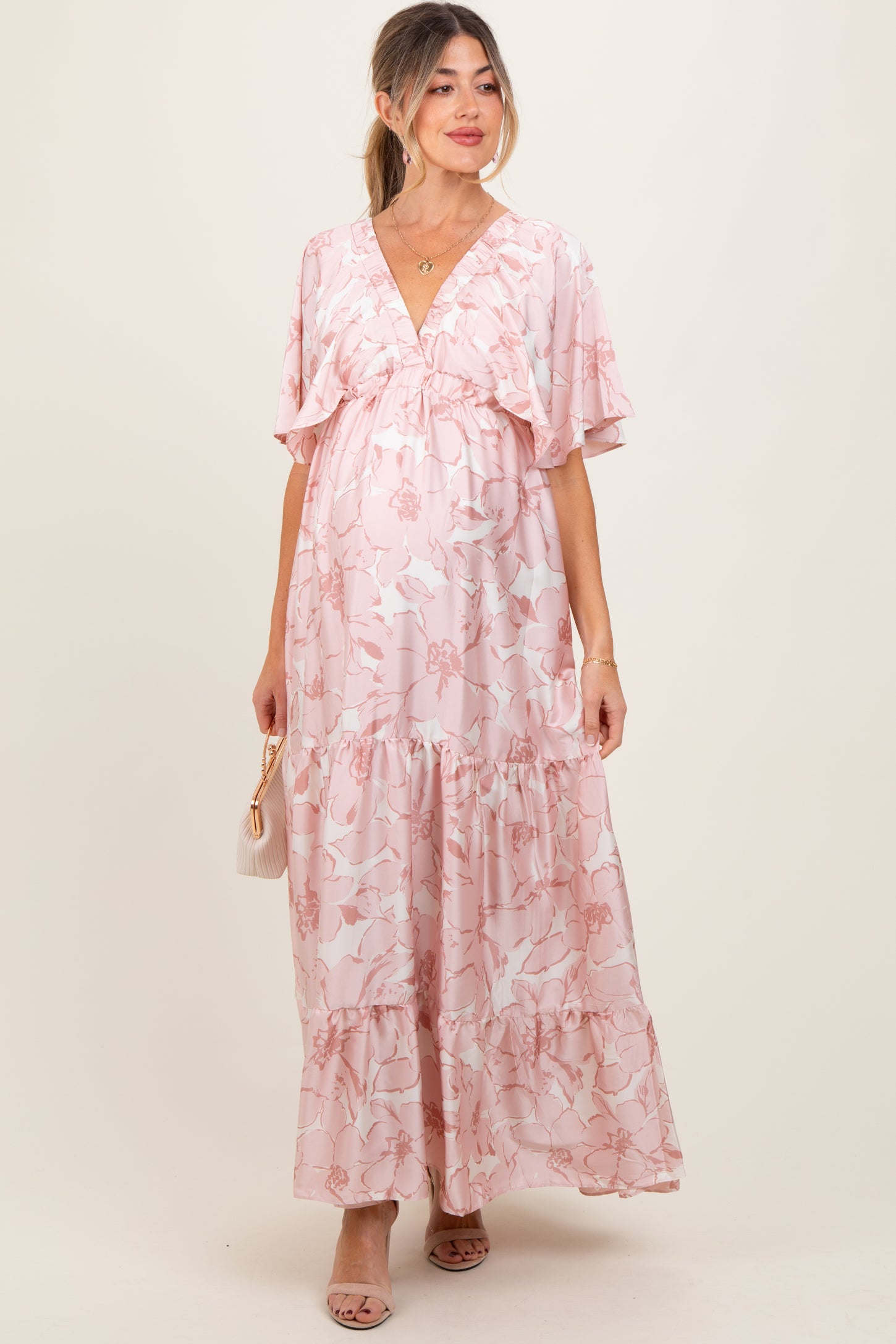 woman wearing a pink floral maternity maxi dress with ruffle sleeves and a flowing skirt, showing her baby bump
