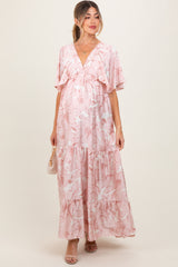 woman wearing a pink floral maternity maxi dress with ruffle sleeves and a flowing skirt, showing her baby bump