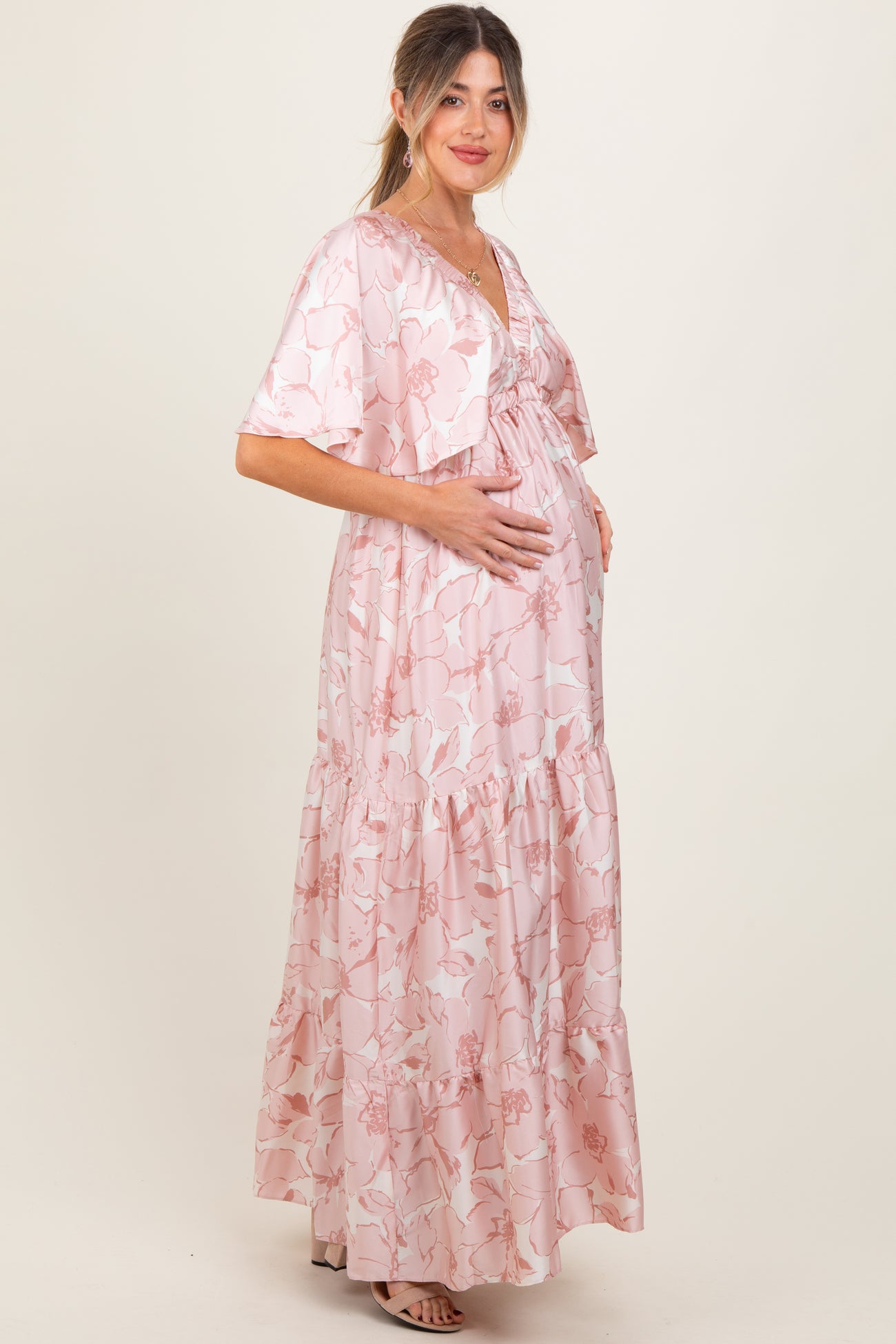 woman wearing a pink floral maternity maxi dress with ruffled tiers and a matching cardigan, holding her baby bump
