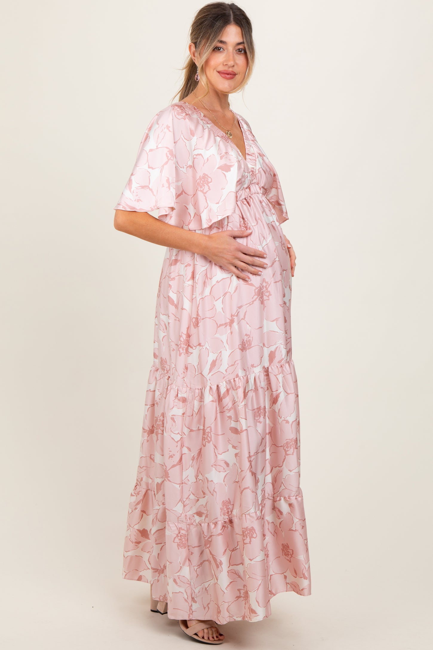 woman wearing a pink floral maternity maxi dress with ruffled tiers and a matching cardigan, holding her baby bump