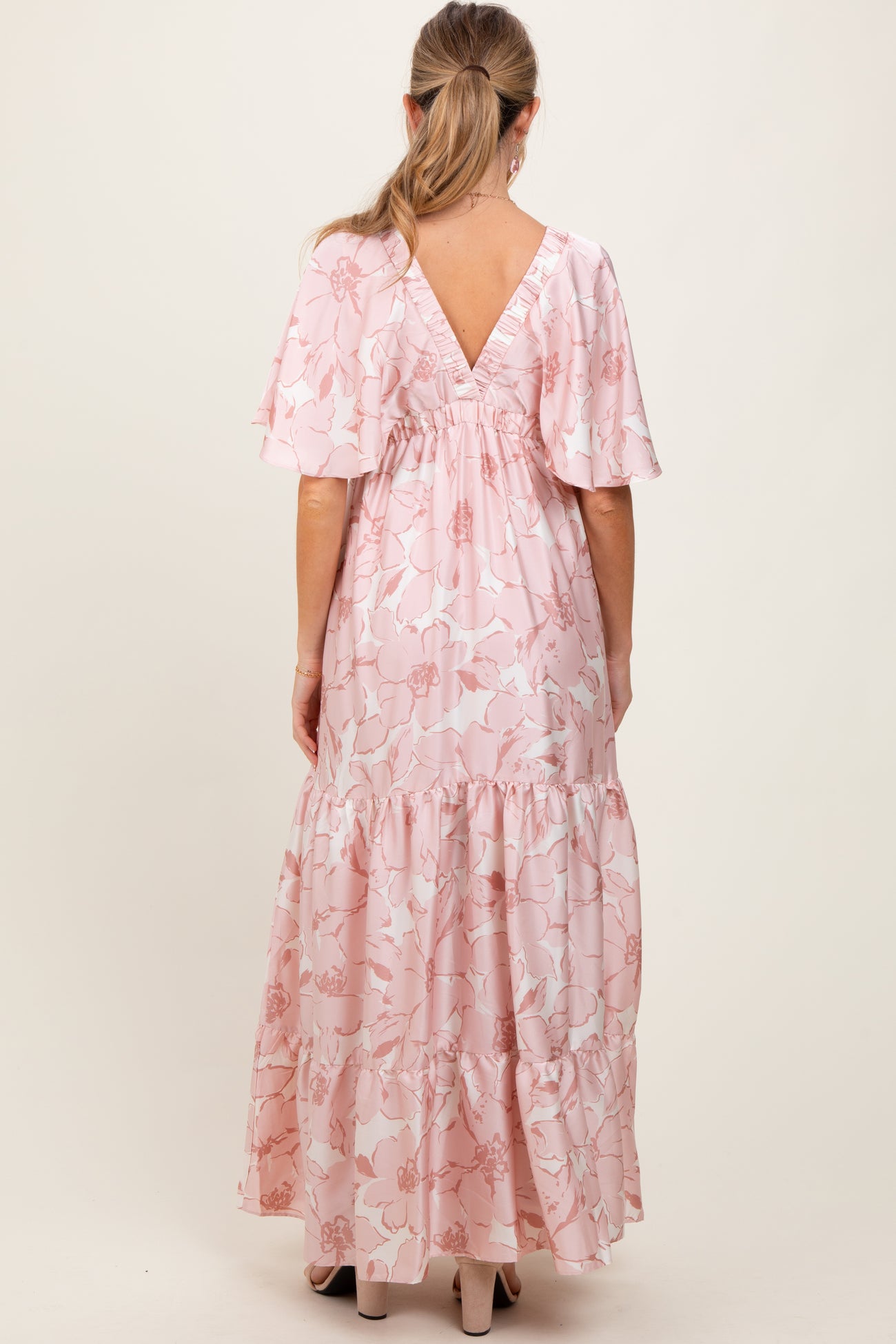 woman wearing a pink floral maternity maxi dress with flutter sleeves and a tiered skirt, showing a v-back design