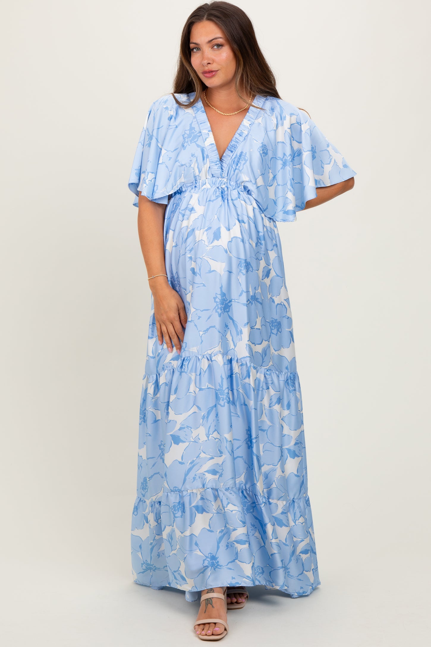 woman wearing a light blue maternity maxi dress with floral print and flutter sleeves, showcasing her baby bump