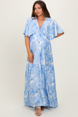 woman wearing a light blue maternity maxi dress with floral print and flutter sleeves, showcasing her baby bump