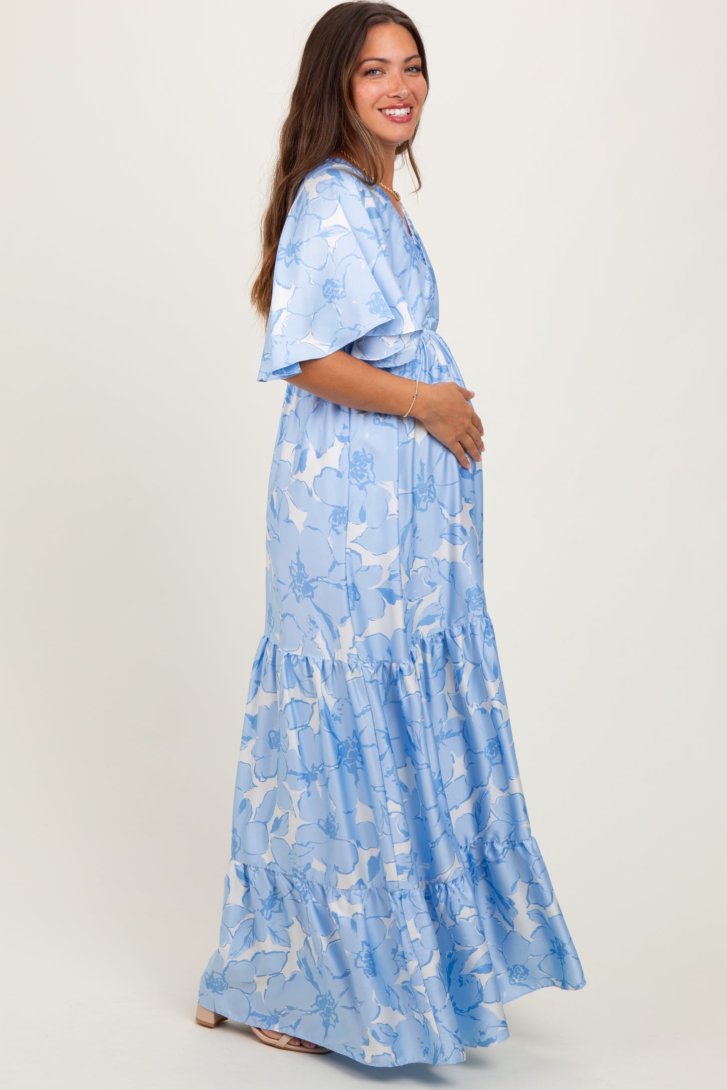woman wearing a light blue floral maternity maxi dress with flutter sleeves and a defined waist, showing her baby bump
