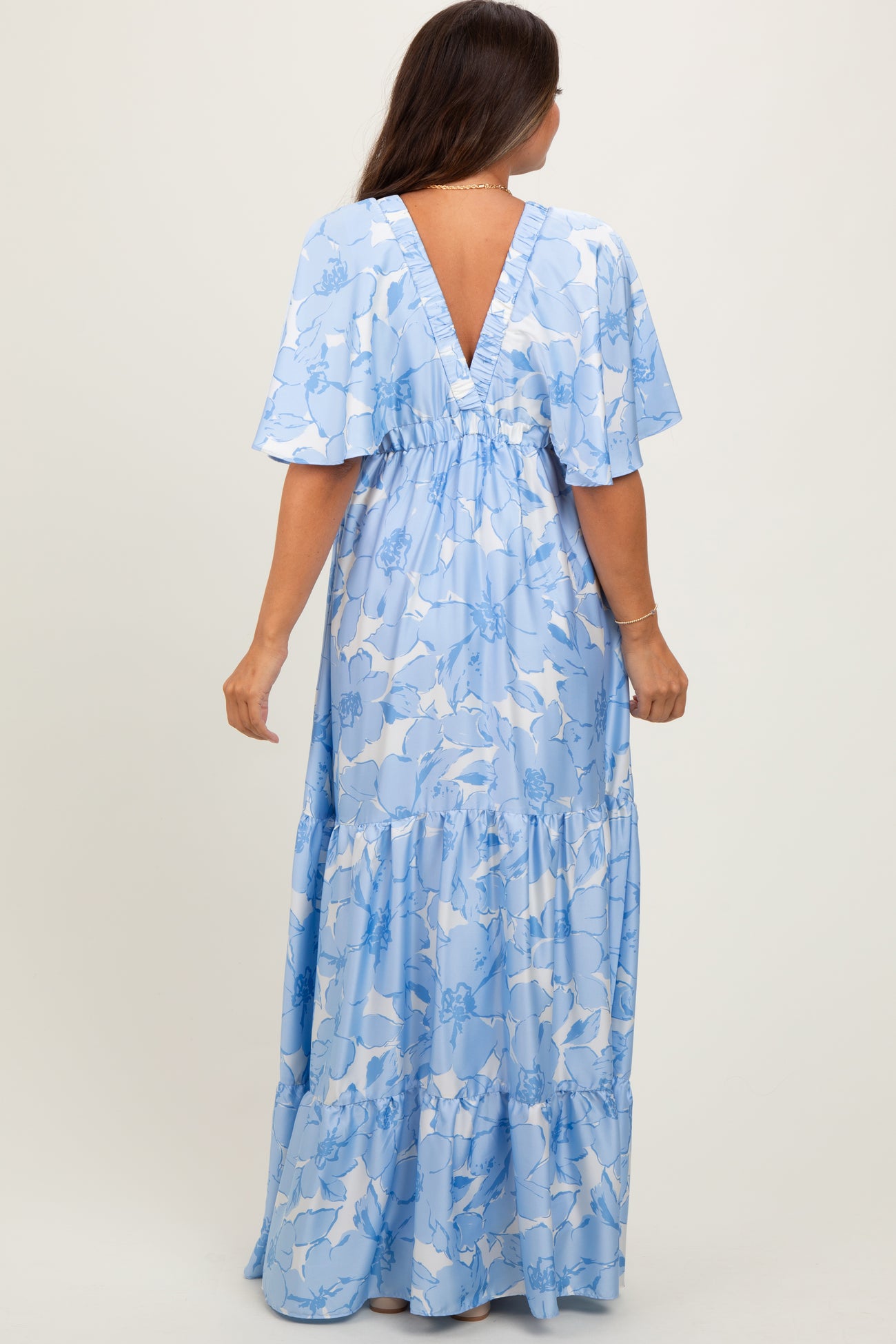 woman wearing a light blue floral maternity maxi dress with a deep V back and short flutter sleeves