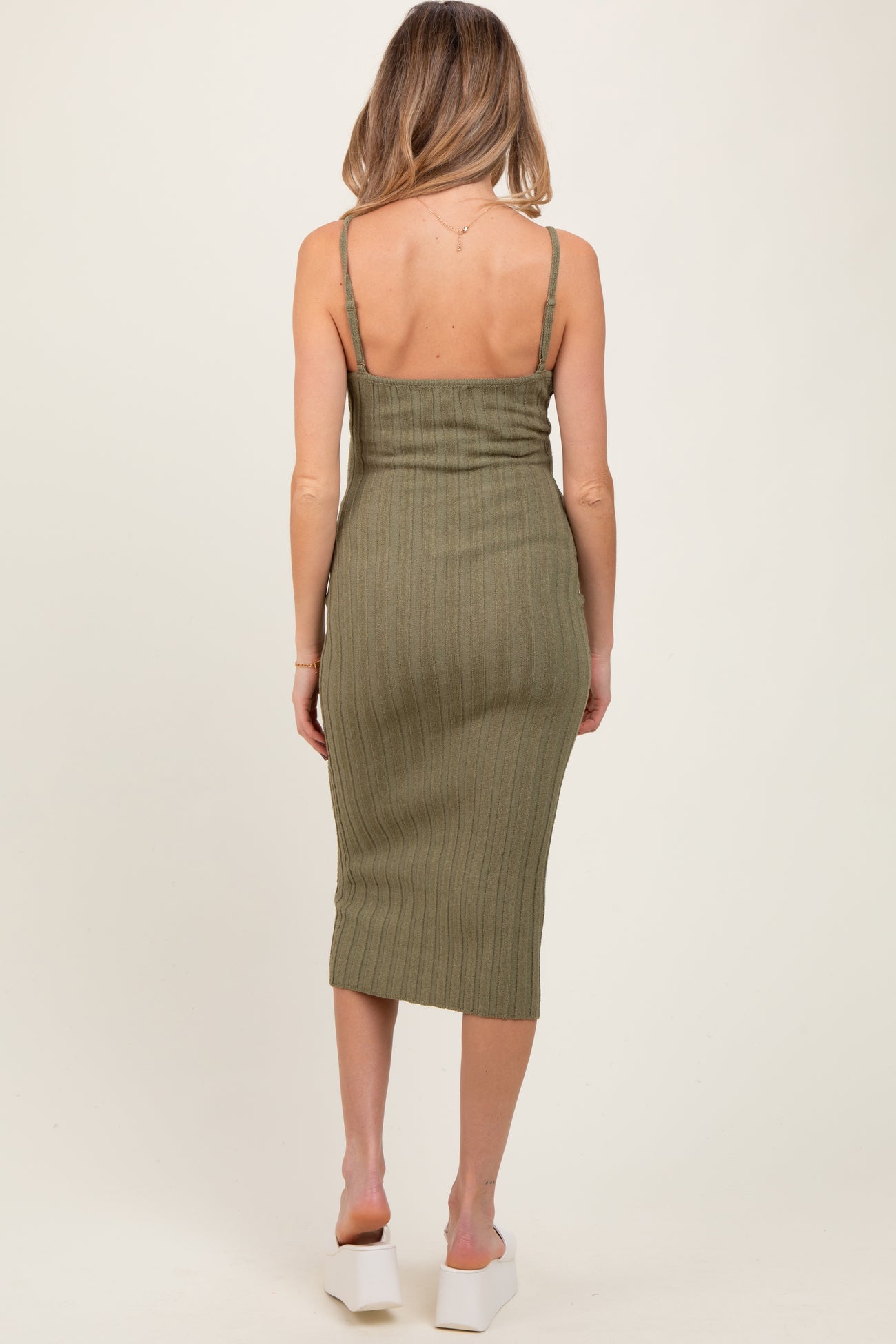 woman wearing an olive green ribbed maternity dress with adjustable straps and a midi length, showing her back