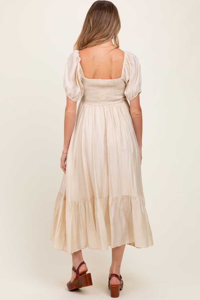 woman wearing a beige maternity dress with puff sleeves and a smocked bodice, showcasing a flowing skirt