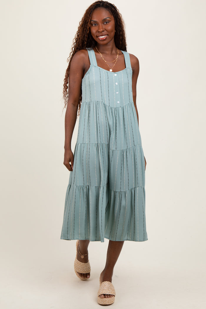 woman wearing a light teal tiered midi dress with adjustable straps and front buttons, standing with a smile