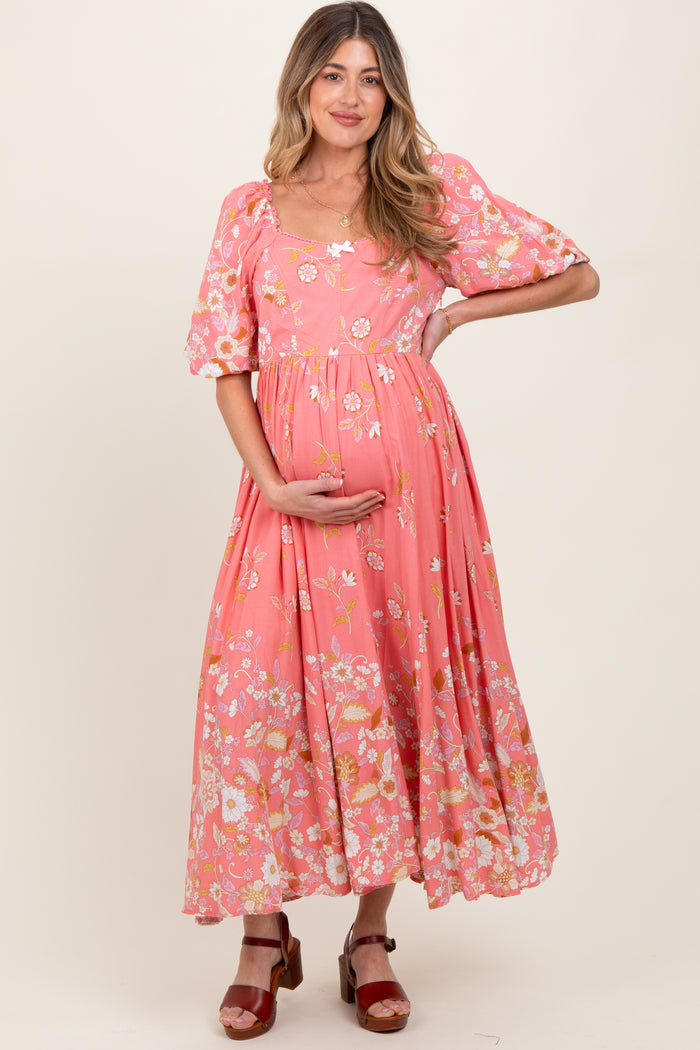 woman wearing a pink floral maternity maxi dress and holding her baby bump