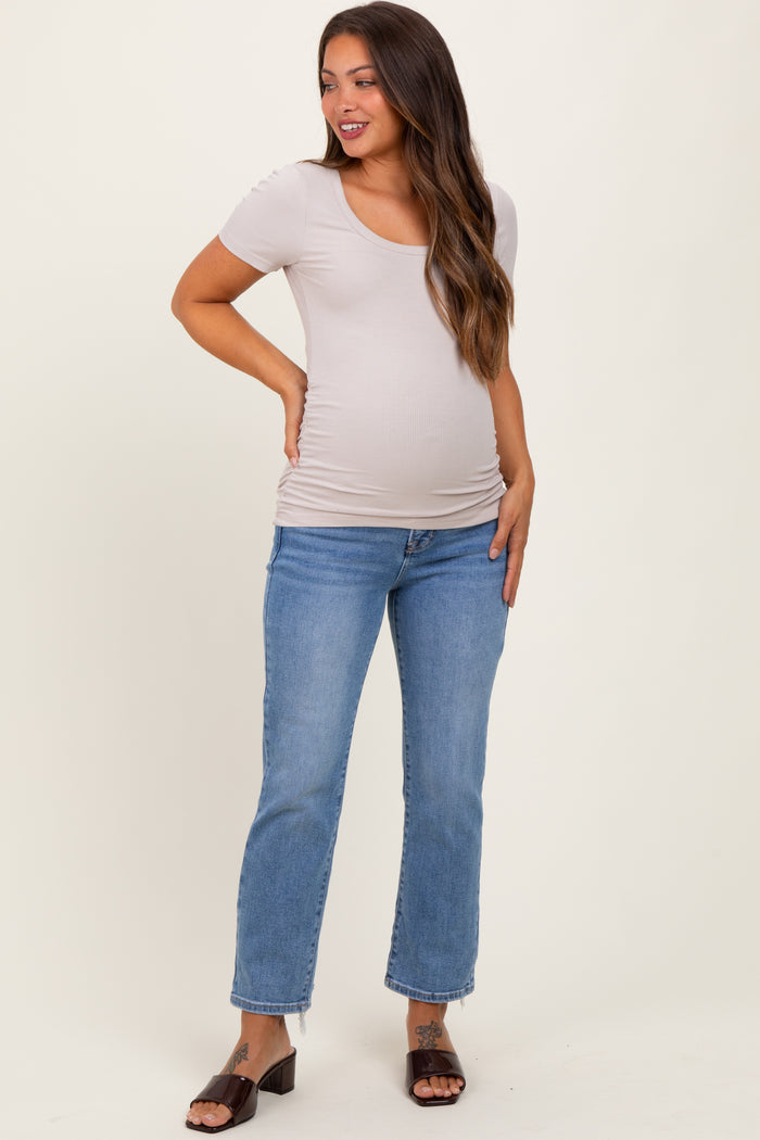 woman wearing a light beige short sleeve maternity top and blue jeans, showing her baby bump