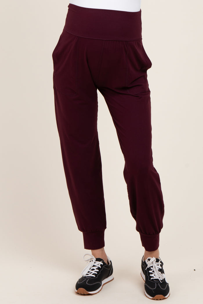 woman wearing burgundy maternity joggers with a wide waistband and tapered cuffs, styled with sneakers
