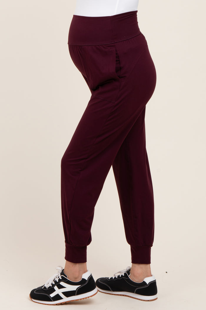 woman wearing burgundy maternity jogger pants with a high waistband and side pockets, displaying her baby bump