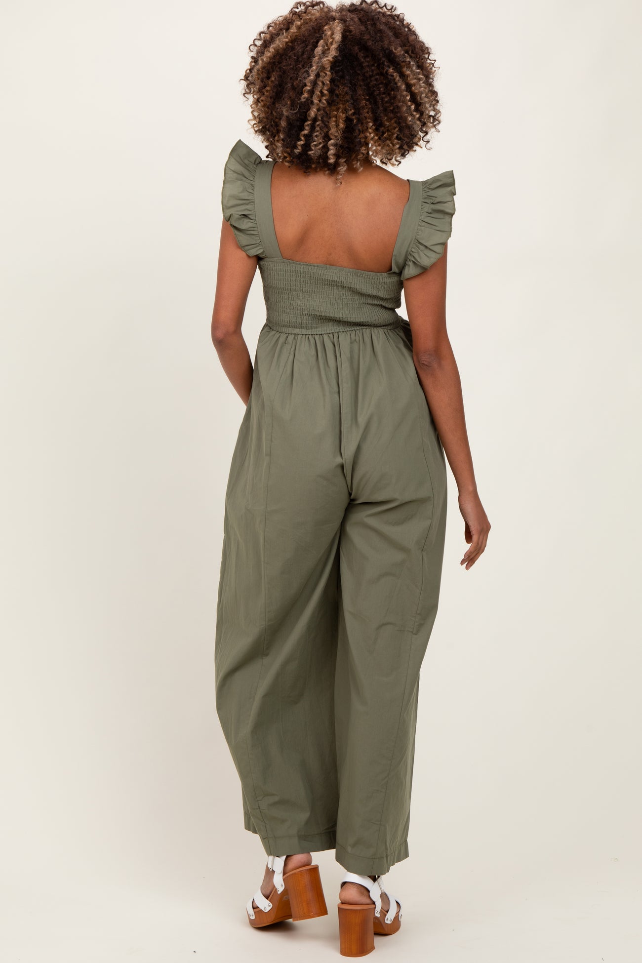 woman wearing an olive green maternity jumpsuit with ruffle sleeves and a smocked back, showing a baby bump