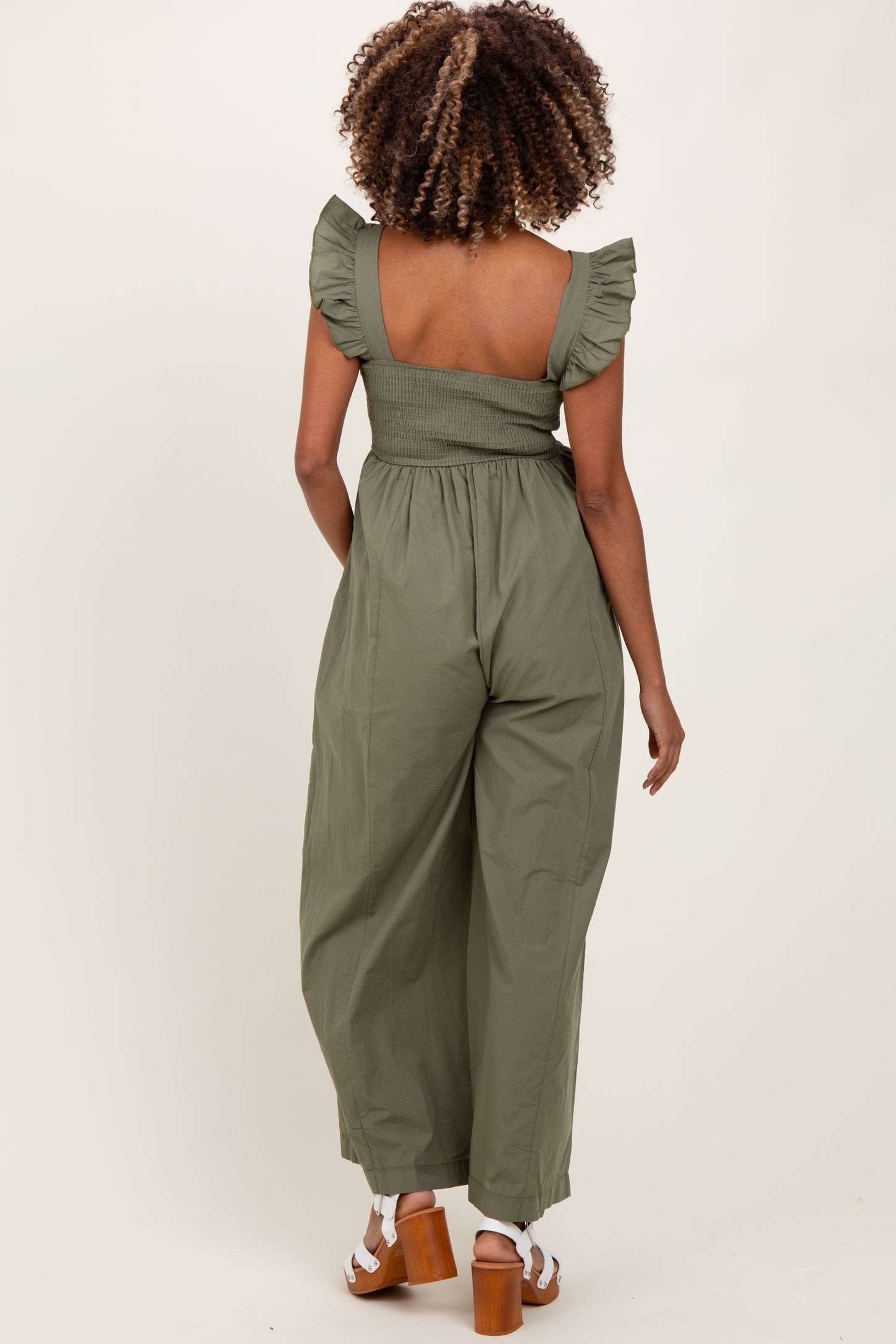 woman wearing an olive green maternity jumpsuit with ruffle sleeves and a smocked back, showing a baby bump