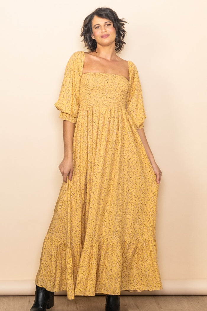 woman wearing a yellow floral maxi dress with puff sleeves and a tiered skirt
