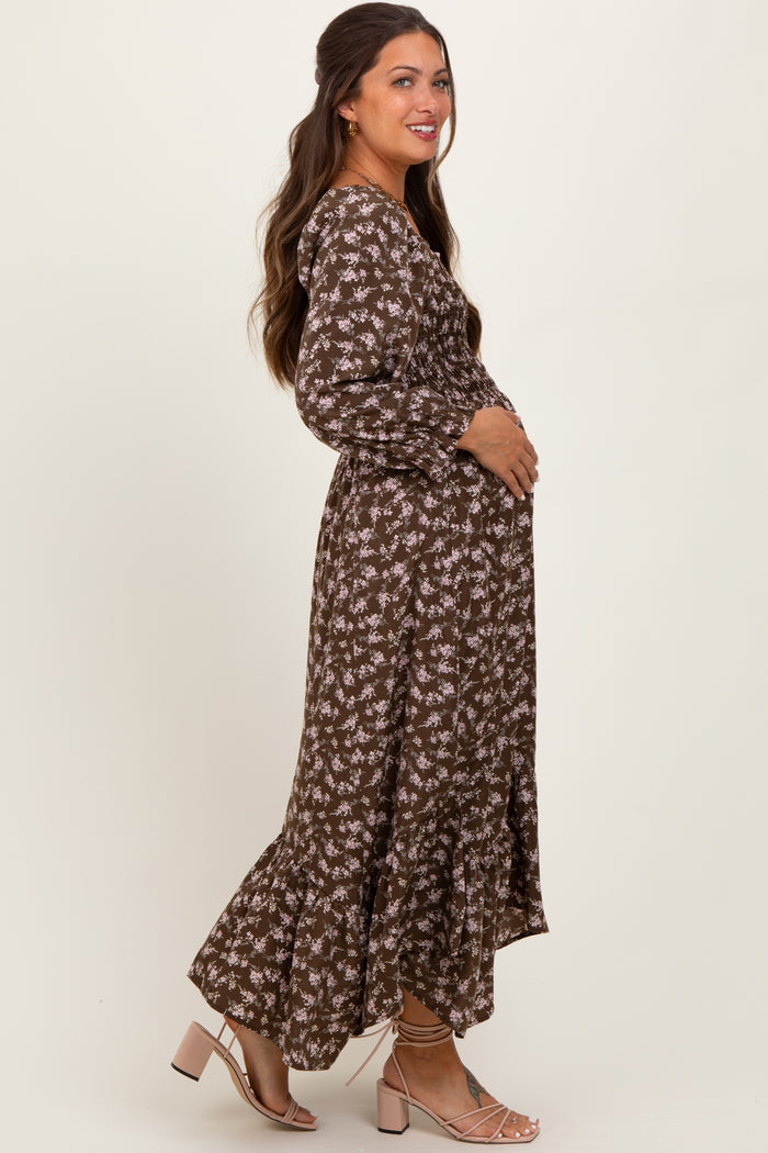 woman wearing a brown floral maternity dress with long sleeves and a ruffled hem, cradling her baby bump