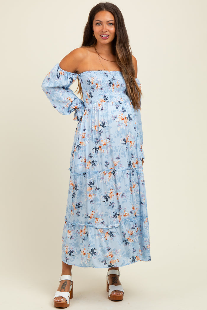 woman wearing a light blue off-shoulder maternity dress with floral print and tiered skirt, no visible baby bump