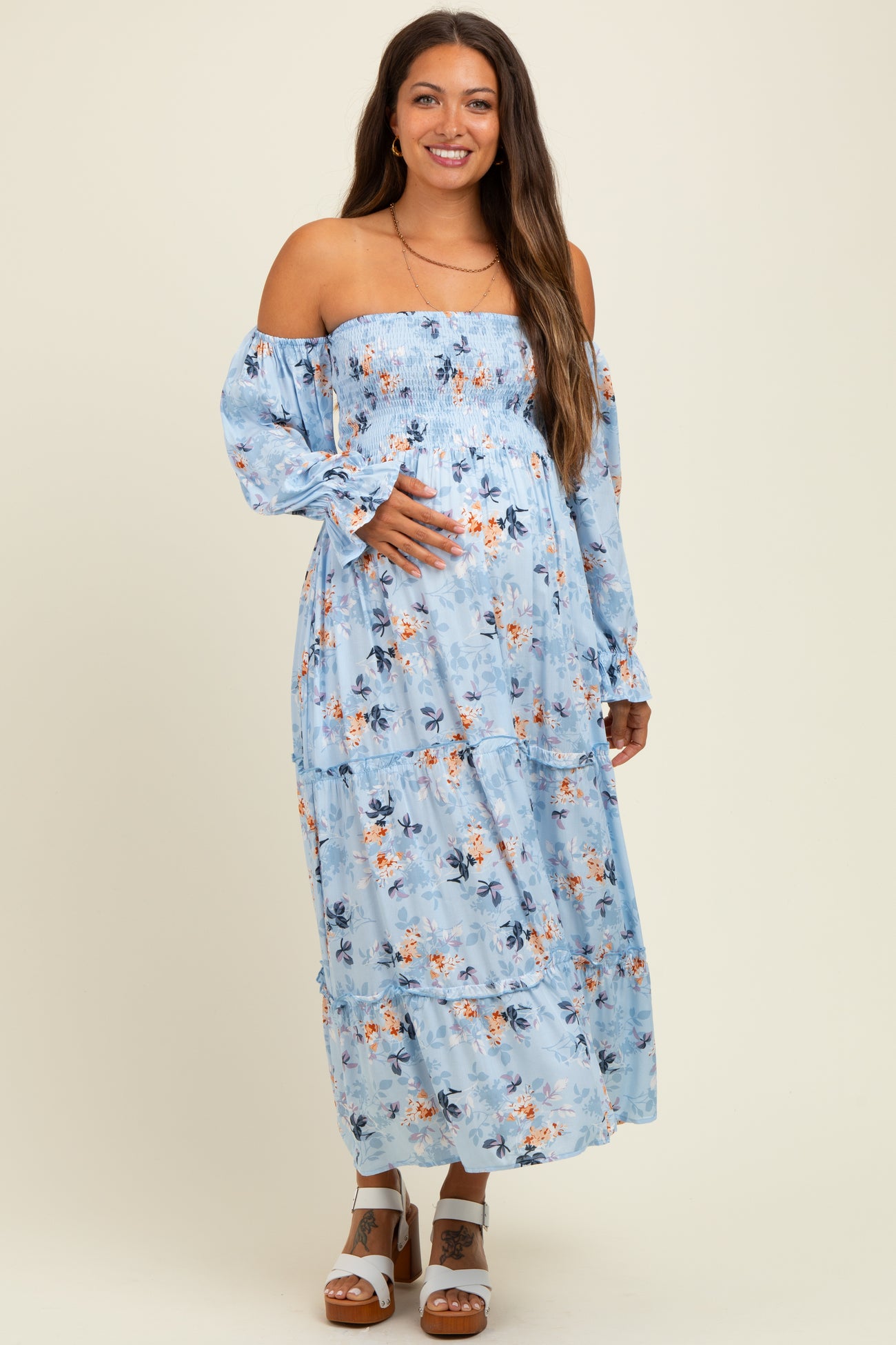 woman wearing a blue floral off-the-shoulder maternity maxi dress and holding her baby bump