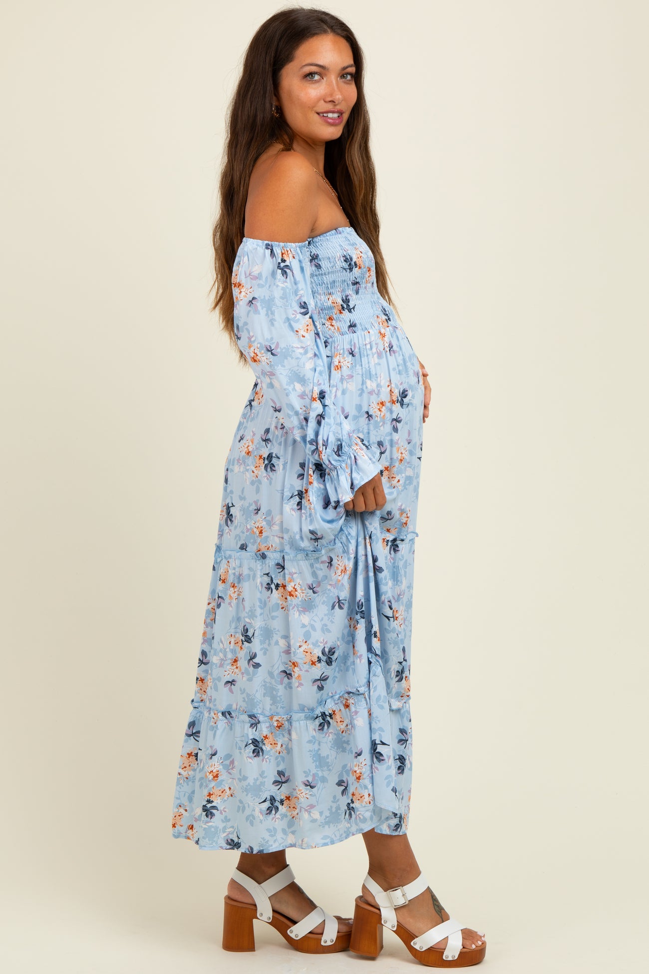 woman wearing a light blue off-the-shoulder maternity dress with floral print and holding her baby bump