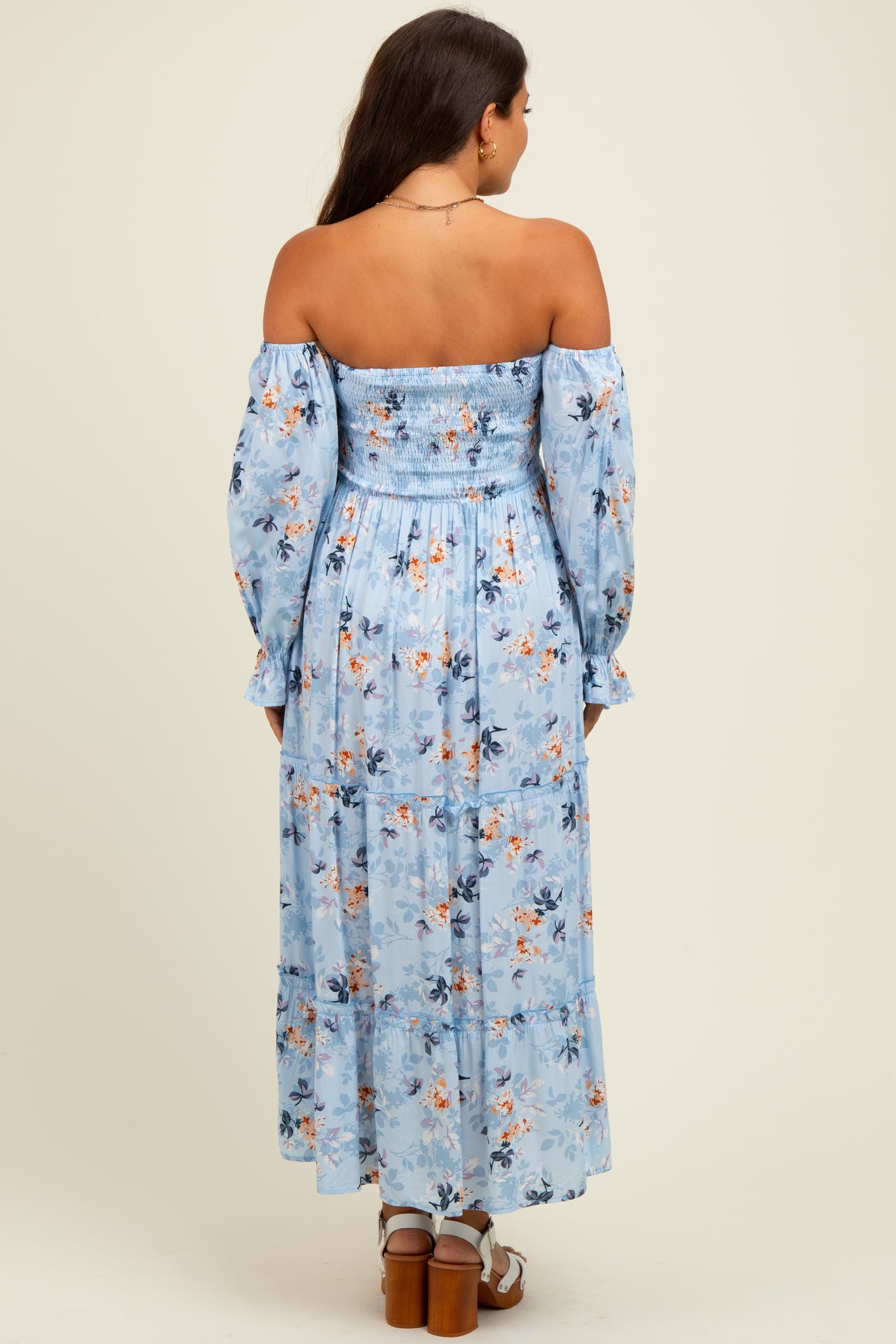 woman wearing a light blue off-the-shoulder maternity dress with floral print and long sleeves, showing a baby bump from behind