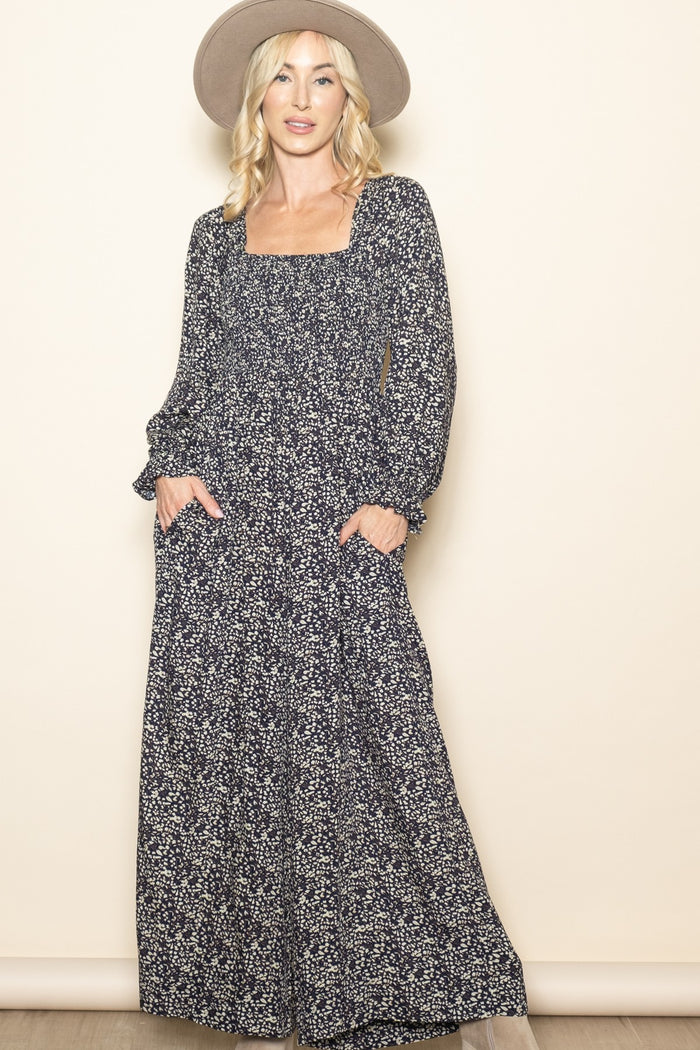 woman wearing a navy blue floral long sleeve maxi dress with a square neckline and pockets, paired with a wide-brim hat