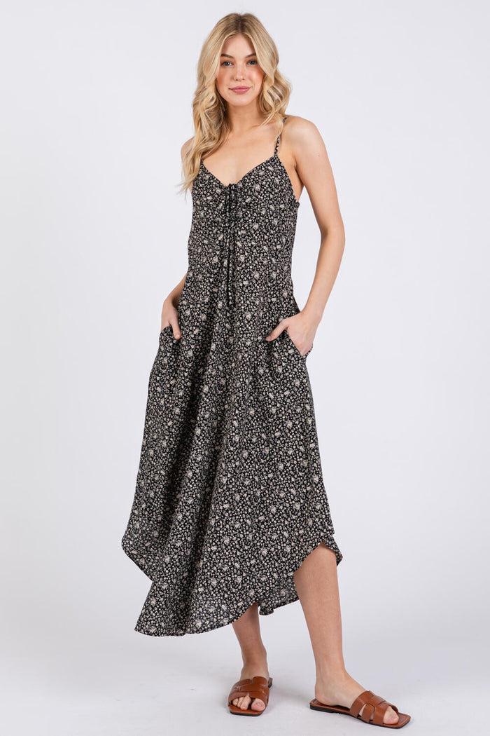 woman wearing a black floral midi dress with adjustable straps and pockets, styled with brown sandals