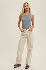 woman wearing a light blue ribbed tank top and cream high-waisted jeans, standing with hands in pockets