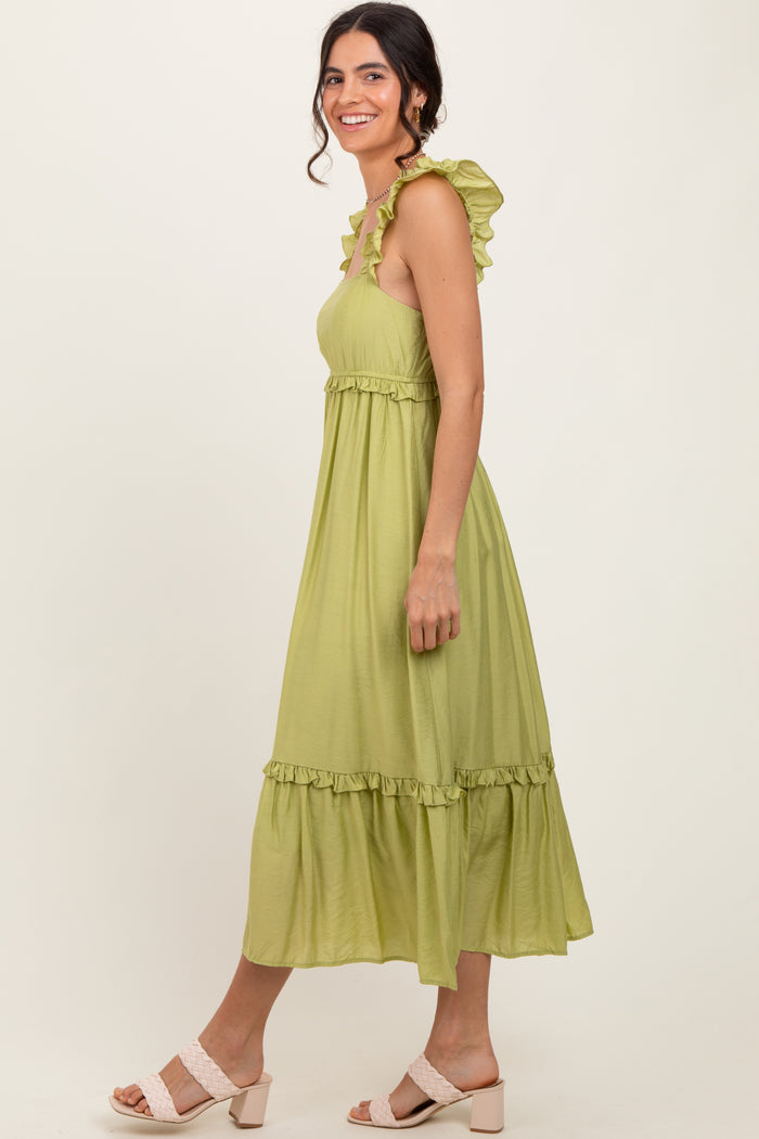 woman wearing a light green sleeveless maxi dress with ruffle straps and a tiered hem, standing sideways