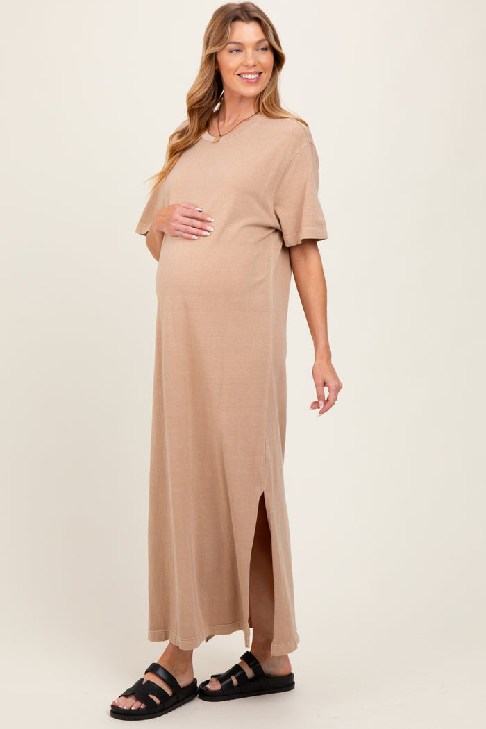 woman wearing a beige short sleeve maternity maxi dress with side slits and holding her baby bump