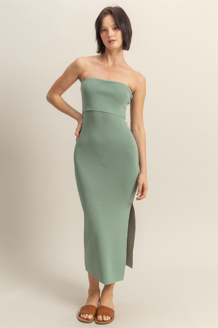 woman wearing a sage green strapless midi dress with a side slit and a fitted silhouette