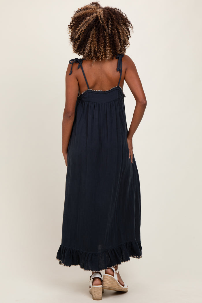 woman wearing a navy blue maternity maxi dress with adjustable straps and ruffled hem, showing off her baby bump