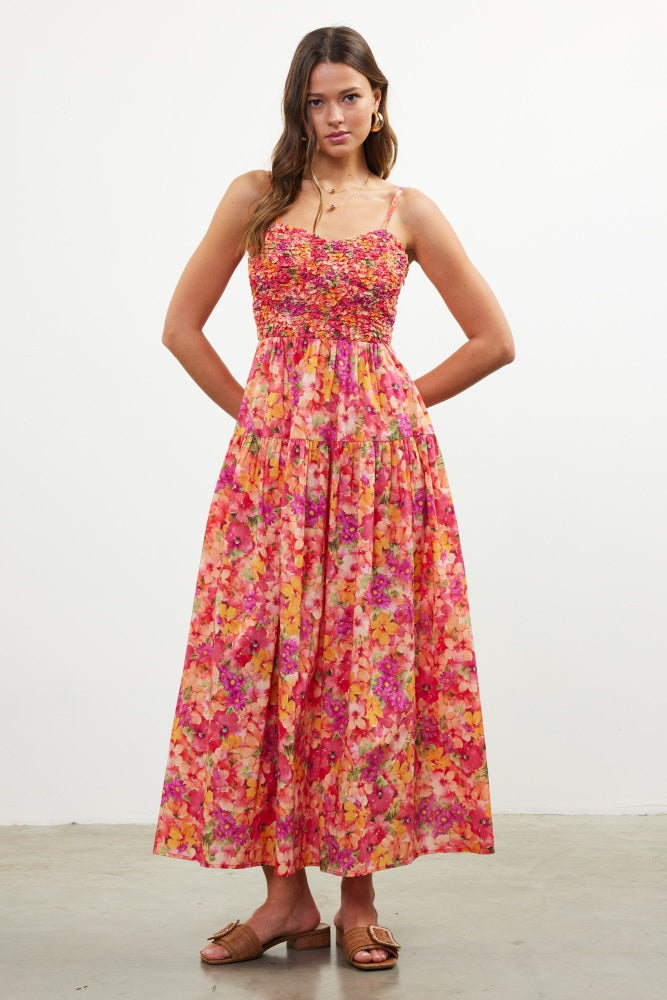 woman wearing a floral pink maxi dress with spaghetti straps and a fitted bodice, standing in a studio setting