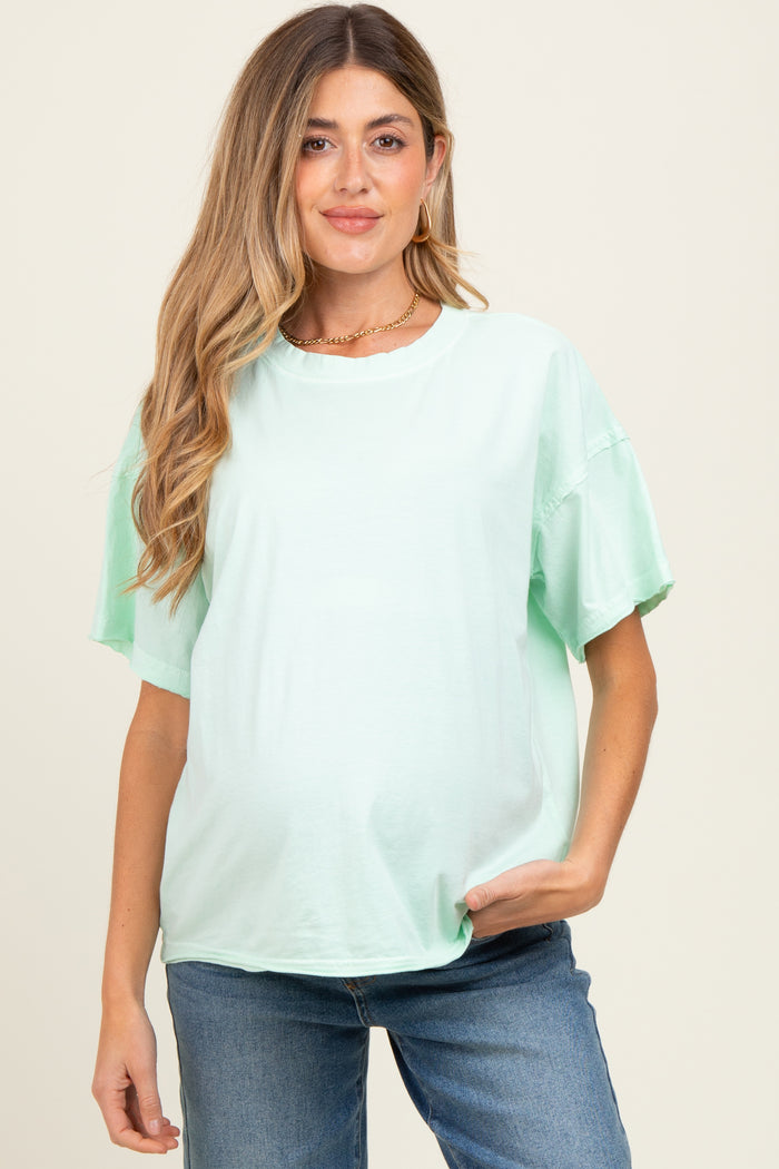 woman wearing a mint green oversized maternity t-shirt and showing her baby bump