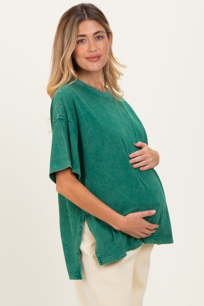 woman wearing a green oversized maternity t-shirt, cradling her baby bump with a smile