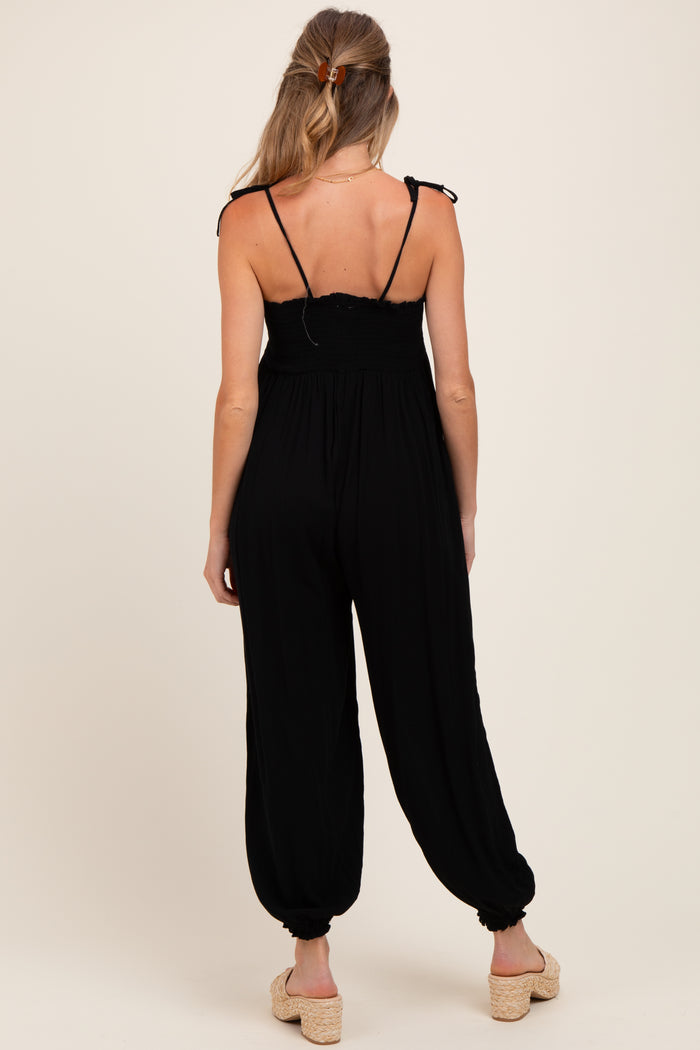 woman wearing a black maternity jumpsuit with smocked bodice and adjustable straps, showing the back view