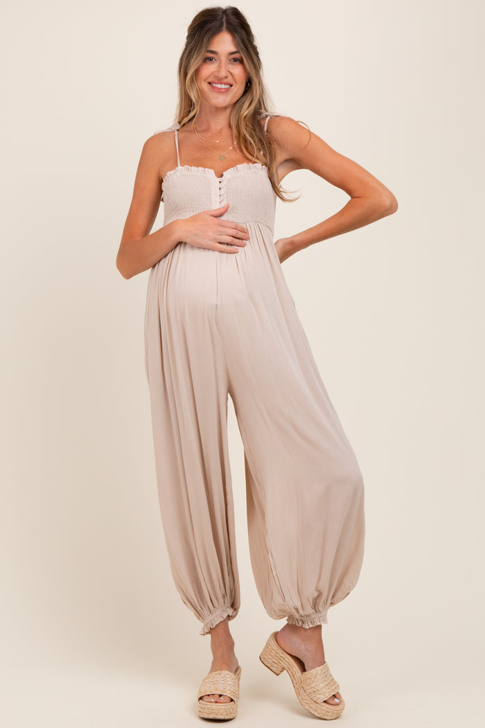 woman wearing a beige maternity jumpsuit with a smocked bodice and balloon legs, showing her baby bump