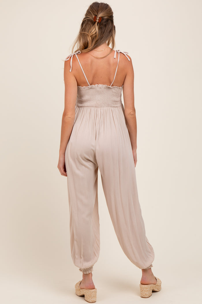 woman wearing a beige maternity jumpsuit with adjustable straps and loose-fitting legs, viewed from the back